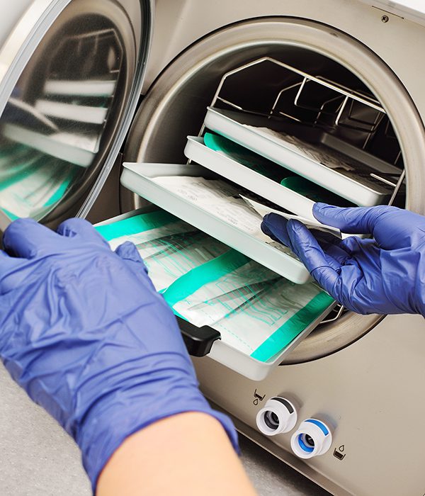 close-up of a doctor's hands in rubber gloves taking sterile instruments out of an autoclave.